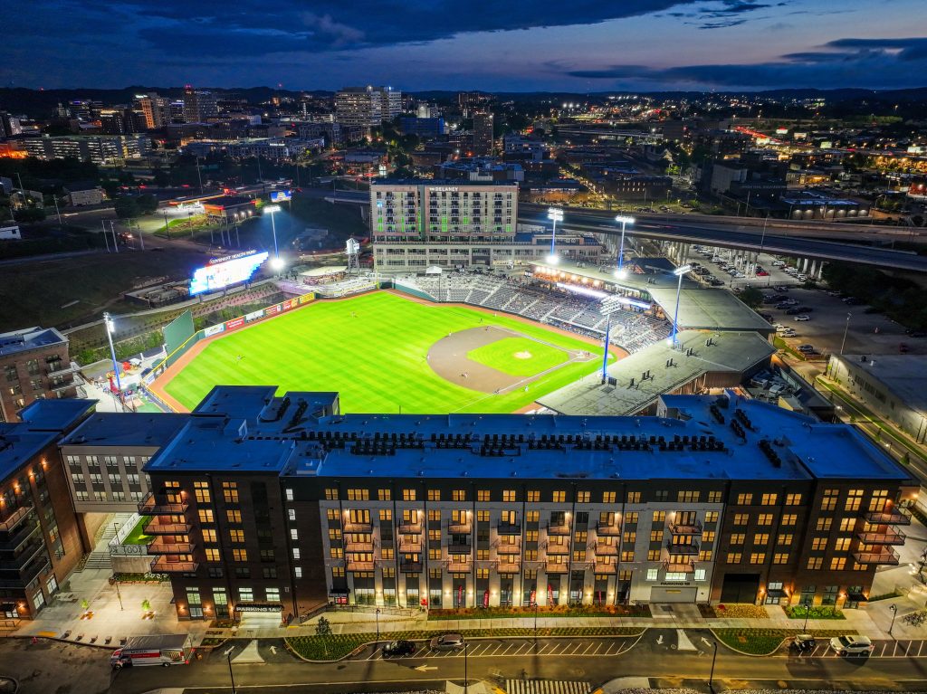 Apartments For Rent Downtown Knoxville Aerial view of a brightly lit baseball stadium at night, surrounded by city buildings and roads, with the city skyline visible in the background. Knoxville Apartments
