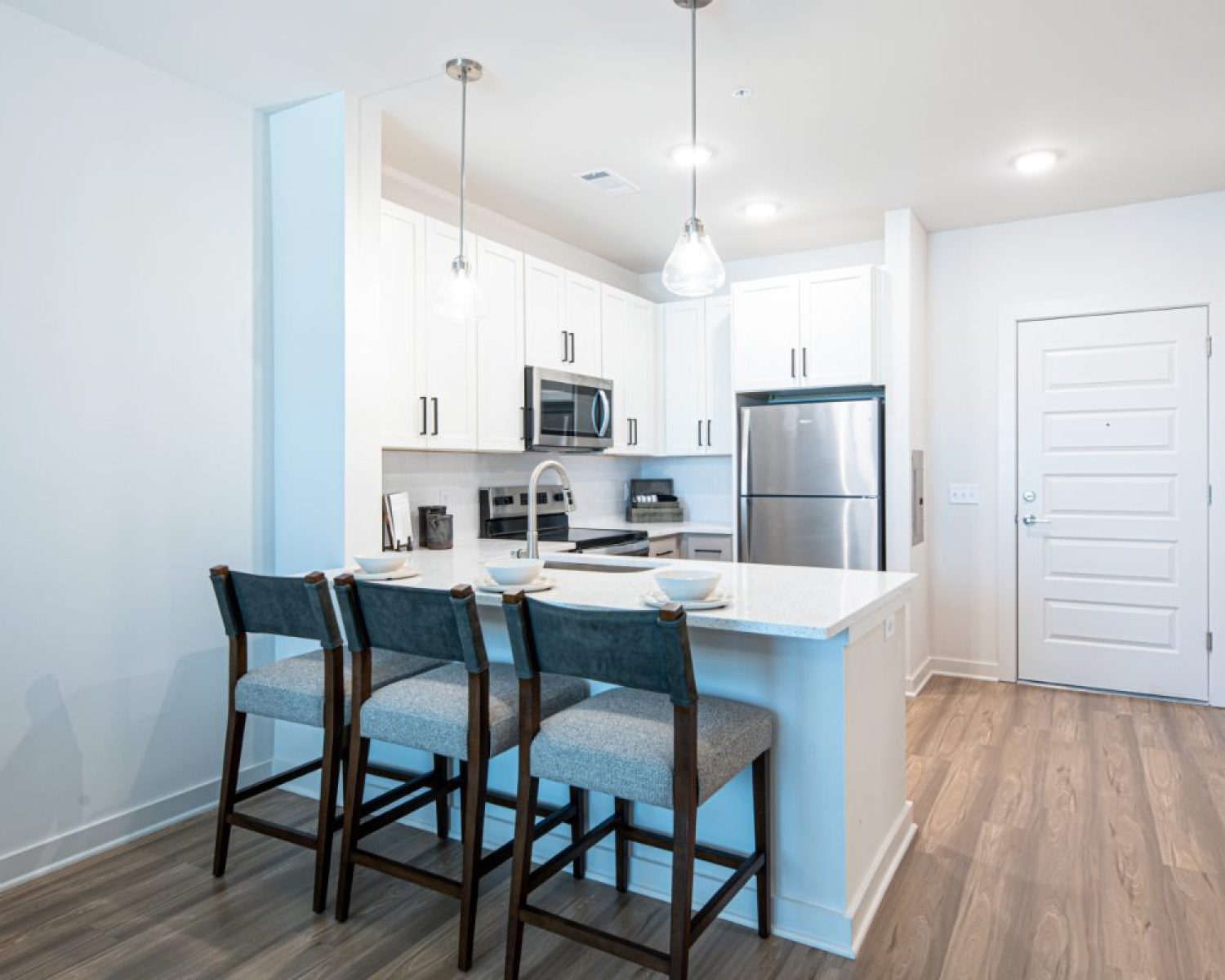 Rental Rates & Deposit Apartments For Rent Downtown Knoxville Modern kitchen with white cabinets, stainless steel appliances, island with three chairs, pendant lighting, and wood flooring. Knoxville Apartments