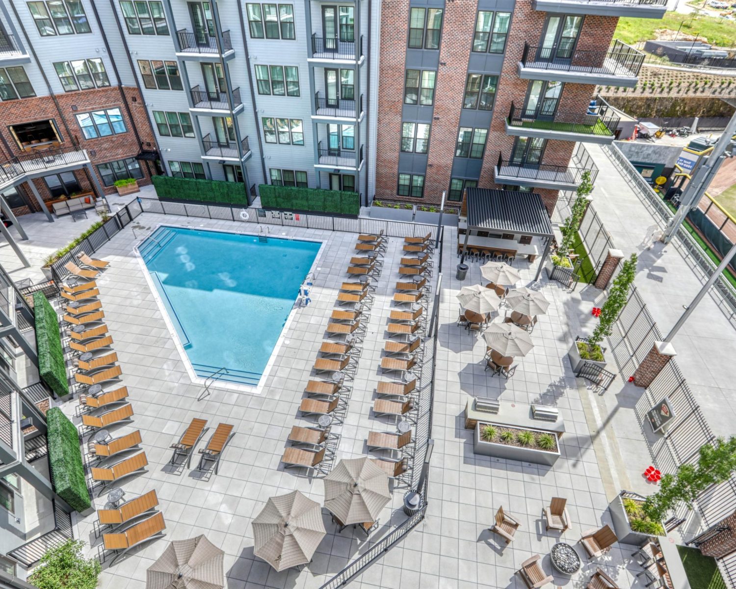 Luxury Apartments Downtown Knoxville Aerial view of an apartment complex courtyard with a rectangular swimming pool, lounge chairs, umbrellas, and surrounding modern buildings. Knoxville Apartments For