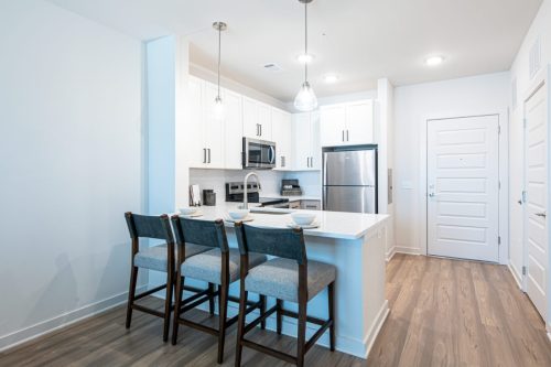 Apartments For Rent Downtown Knoxville Modern kitchen with white cabinets, stainless steel appliances, island with three chairs, pendant lighting, and wood flooring. Knoxville Apartments