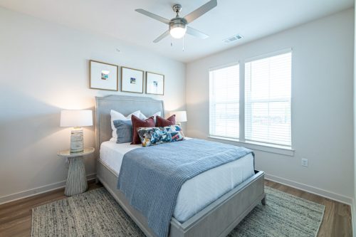Apartments For Rent Downtown Knoxville A modern bedroom with a neatly made bed, decorative pillows, two bedside tables with lamps, framed art above the headboard, and large windows letting in natural light. Knoxville Apartments
