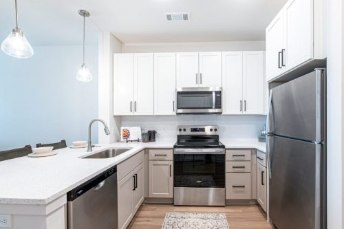 Apartments For Rent Downtown Knoxville Modern kitchen with white cabinets, stainless steel appliances, electric range, dishwasher, microwave, refrigerator, and pendant lights above a countertop with a sink. Knoxville Apartments